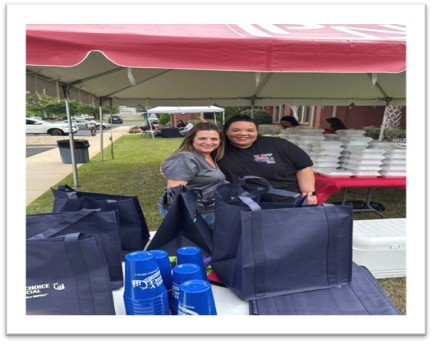 two women handing out food under a tent